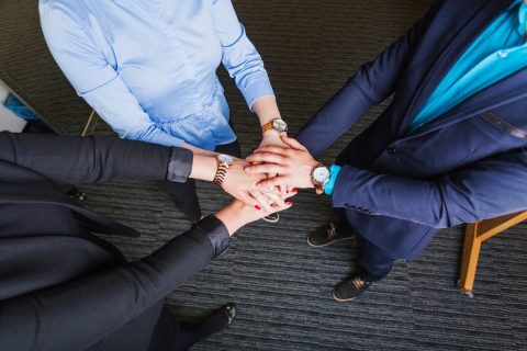 people-standing-office-holding-hands-together_23-2147650946